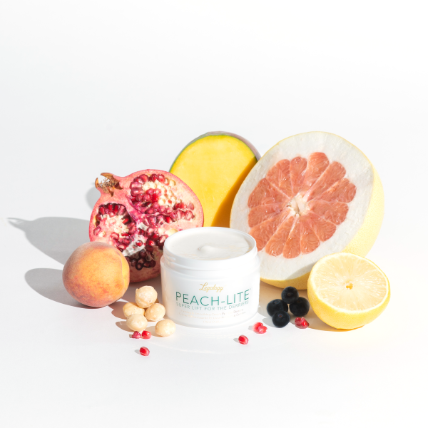 A white pot of cream with green text and a gold logo. The logo reads Legology. The product is called Peach-Lite Super Lift For The Derriere. It is sat in the middle of a display of citrus fruits, blueberries and a pomegranate.